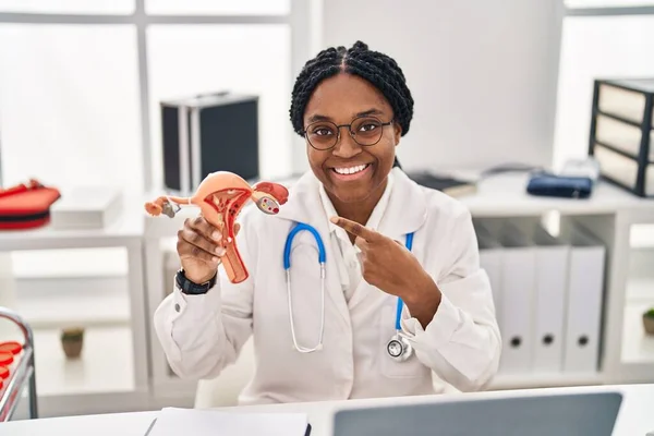 African american doctor woman holding anatomical model of female genital organ smiling happy pointing with hand and finger
