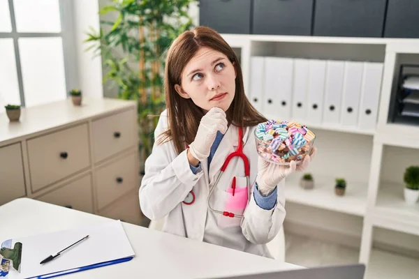 年轻的女医生抱着糖果严肃的脸 手托着下巴思考着问题 沉思着困惑的想法 — 图库照片