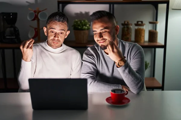Homosexual couple using computer laptop doing italian gesture with hand and fingers confident expression