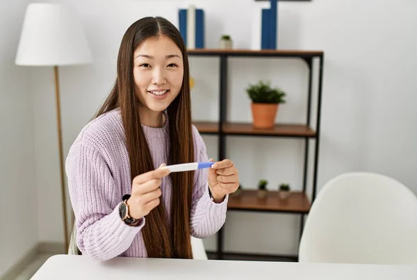 若いです中国の女の子保持妊娠テスト座っていますザテーブルの上にホーム — ストック写真