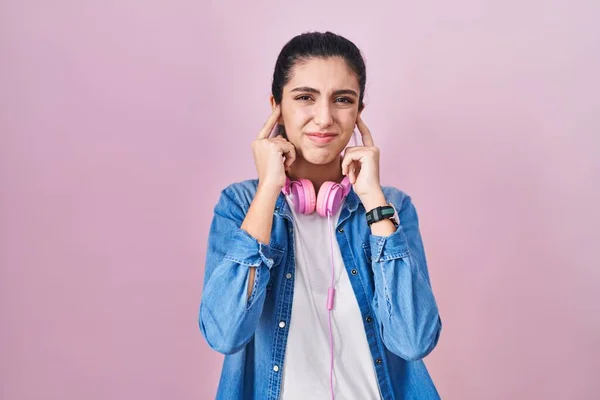 ピンクの背景に立つ若い美少女は 大きな音楽のノイズに悩まされた表情で指で耳を覆います 聴覚障害の概念 — ストック写真