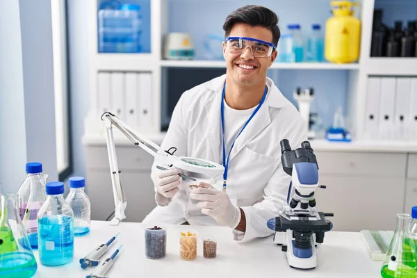 Young hispanic man scientist looking sample with loupe at laboratory