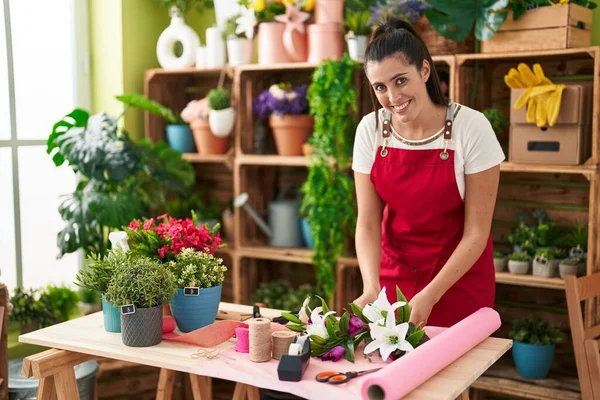 Young beautiful hispanic woman florist make bouquet of flowers at flower shop