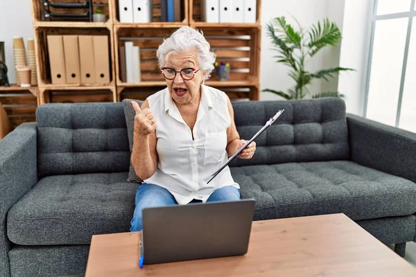 在咨询处工作的白发苍苍的老年妇女正在做在线治疗 指尖着大拇指朝边笑着 嘴角张开得很开心 — 图库照片