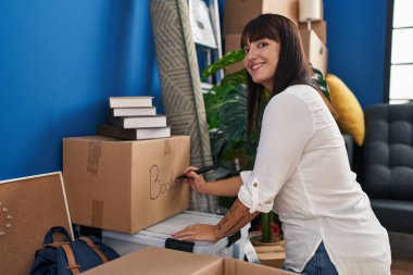 Genç, güzel, İspanyol bir kadın gülümsüyor. Yeni evinde pakete kitap yazıyor.