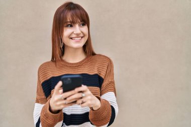 Sokakta akıllı telefon kullanan kendine güvenen genç bir kadın.