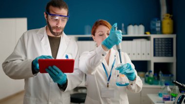 Laboratuvarda dokunmatik ped kullanan bilim adamı ve kadın üniforması giyiyor.