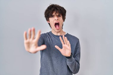 Young man standing over isolated background afraid and terrified with fear expression stop gesture with hands, shouting in shock. panic concept. 
