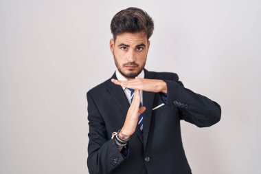 Young hispanic man with tattoos wearing business suit and tie doing time out gesture with hands, frustrated and serious face 