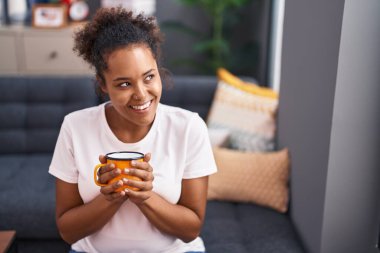 African american woman drinking coffee sitting on sofa at home