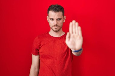 Kırmızı arka planda duran İspanyol genç adam avucunun içi gibi şarkı söylemeyi kesiyor. Yüzünde olumsuz ve ciddi bir jest olan uyarı ifadesi. 