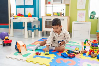 Adorable hispanic toddler playing with car toy sitting on floor at kindergarten