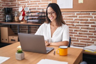 Hispanic young woman working at the office wearing glasses with a happy and cool smile on face. lucky person. 