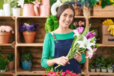 Young beautiful hispanic woman florist holding bouquet of flowers at flower shop