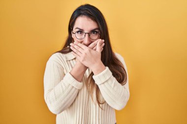 Sarı arka planda duran genç İspanyol kadın yanlışlıkla ağzı ellerle kapatırken şok oldu. gizli kavram. 