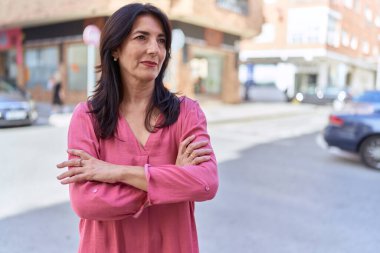 Orta yaşlı İspanyol kadın caddede kollarını kavuşturup el kol hareketi yapıyor.