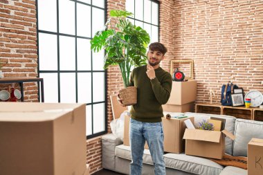 Young arab man smiling confident holding plant at new home