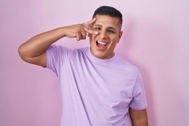Pembe arka planda duran genç İspanyol adam barış sembolü yapıyor. Yüzünde parmakları, gülümseyerek zaferi gösteriyor. 