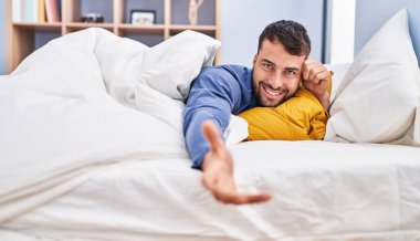 Young hispanic man shake hand lying on bed at bedroom