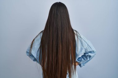 Mavi arka planda dikilen genç İspanyol kadın geriye bakıyor kolları vücudunda. 