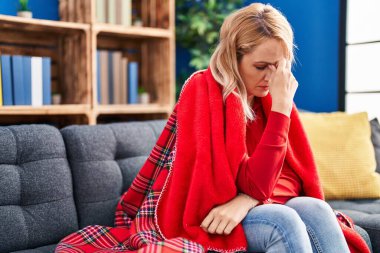 Evdeki kanepede oturan genç sarışın kadın baş ağrısı çekiyor.