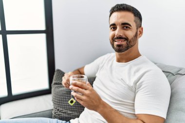 Young hispanic man smiling confident drinking tea at home