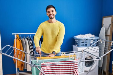 Genç İspanyol adam gülümsüyor. Çamaşır odasında kendine güveni tam bir elbise asıyor.