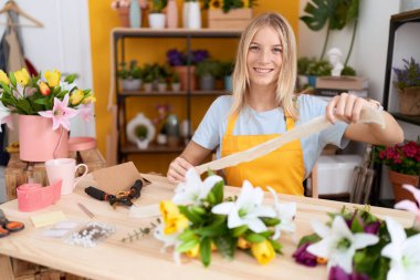 Çiçekçi dükkanında kendine güvenen genç sarışın kadın dantel tutuyor.