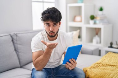 Dokunmatik ped kullanan İspanyol sakallı bir adam koltukta oturmuş kameraya bakıyor ve havada bir öpücük savuruyor. Güzel ve seksi. aşk ifadesi. 