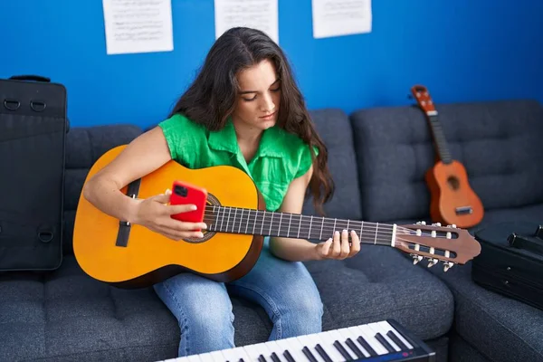 若いヒスパニック系の女性音楽家が音楽スタジオでスマートフォンを使ってクラシックギターを演奏 — ストック写真