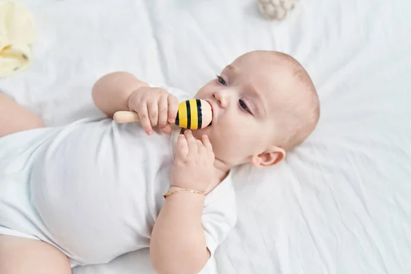 Liebenswertes Kaukasisches Baby Liegt Auf Bett Und Lutscht Maraca Spielzeug — Stockfoto