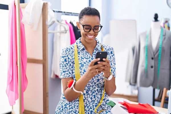 African american woman tailor smiling confident using smartphone at tailor shop