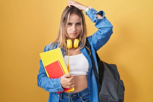 年轻的金发女子背着学生背包 拿着书本 对问题感到困惑和疑惑 拿不定主意 手拿着头思考 沉思的概念 — 图库照片
