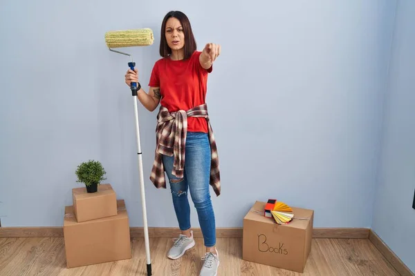 Young Hispanic Woman Painting Home Walls Paint Roller Pointing Displeased — Stockfoto