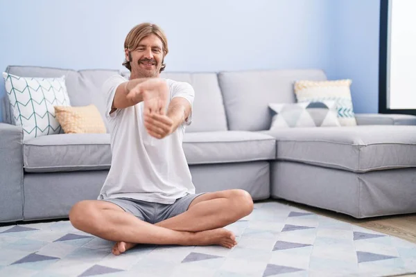 Young blond man smiling confident stretching arm at home