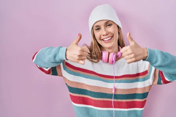 Young blonde woman standing over pink background approving doing positive gesture with hand, thumbs up smiling and happy for success. winner gesture.
