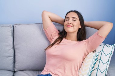 Genç, güzel, İspanyol bir kadın. Elleri başının üstünde, evdeki kanepede oturuyor.