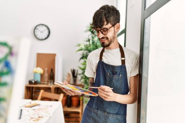 Genç İspanyol ressam mutlu bir şekilde resim stüdyosunda duruyor..