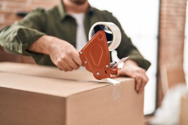 Genç beyaz adam yeni evinde karton kutu paketliyor.