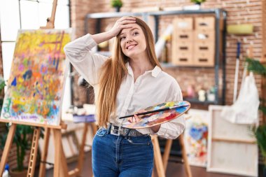 Young caucasian woman at art studio holding palette stressed and frustrated with hand on head, surprised and angry face 