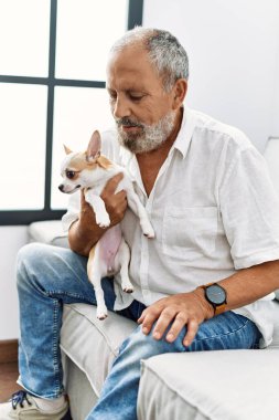 Yaşlı, gri saçlı, gülümseyen ve elinde Chihuahua tutan adam.