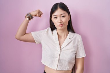 Pembe arka planda duran Çinli genç bir kadın güçlü bir insan kol kası gösteriyor, kendinden emin ve gururlu. 