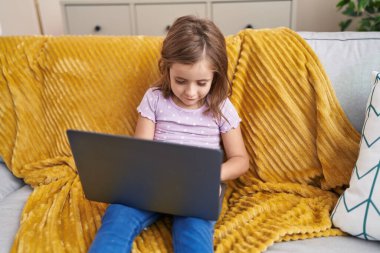 Adorable hispanic girl using laptop sitting on sofa at home