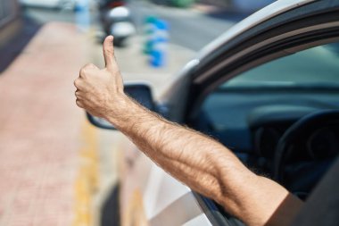 Young caucasian man driving car doing ok gesture with thumb up at street