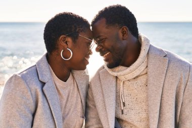 Kadın ve erkek, sırıtıyor. Sahilde oturuyorlar.