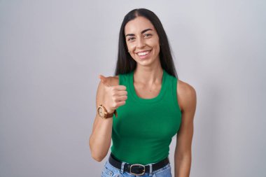 Young woman standing over isolated background doing happy thumbs up gesture with hand. approving expression looking at the camera showing success. 