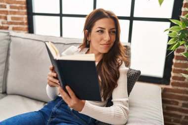 Evdeki kanepede oturmuş kitap okuyan genç İspanyol kadın.