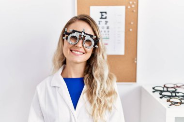 Klinikte optometri gözlüğü takan genç ve güzel gözlüklü bir kadın pozitif ve mutlu görünüyor ve kendine güvenen bir gülümsemeyle dişlerini gösteriyor. 