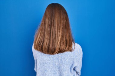 Young woman standing over blue background standing backwards looking away with crossed arms 