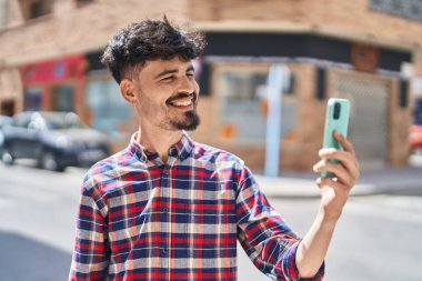 Genç İspanyol adam gülümsüyor. Sokakta akıllı telefonun yanında özçekim yapıyor.